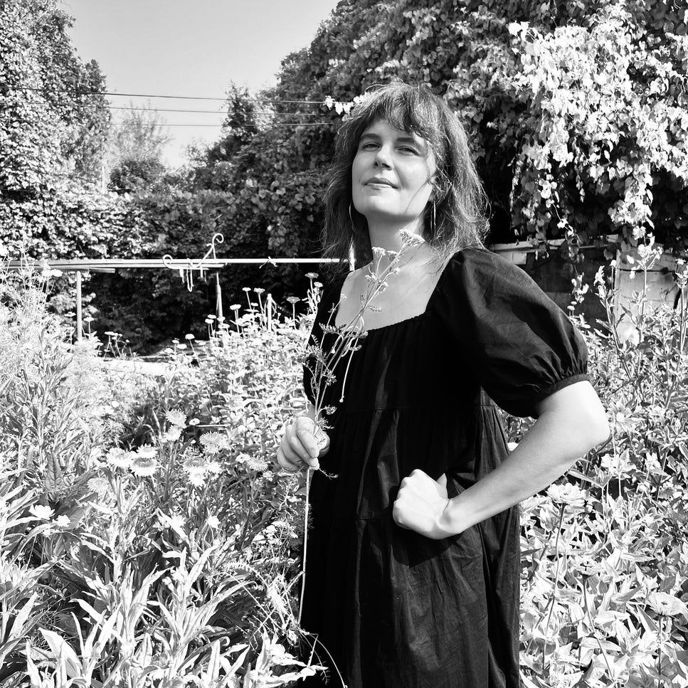 Ash Posy founder Andrea in a black dress standing in a garden with trees and plants in the background