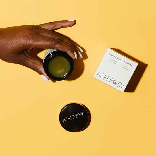 A manicured dark-skinned hand holds a tub of Ash Posy Supernatural Jelly Balm