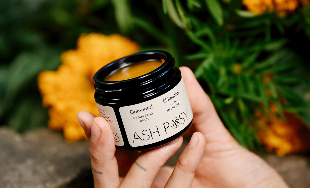 Person holding a jar of 'Elemental' balm with flowers in the background