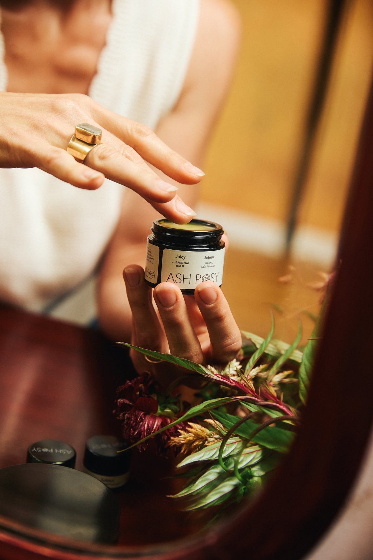 A person sits in front of a mirror scooping some Juicy Cleansing Balm out of the tub.